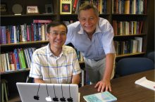 Professors Q. Charles Su and Rainer Grobe work at a laptop in front of rows of books